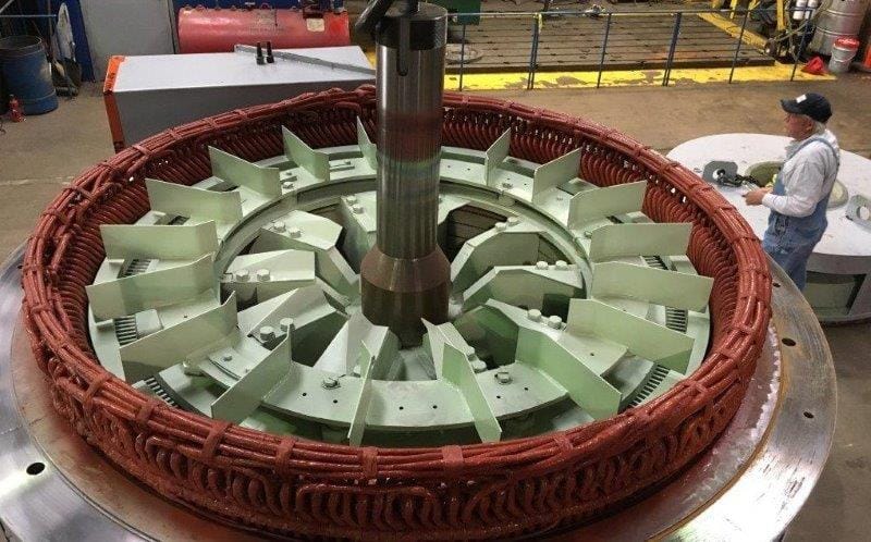 A 26-pole circulating water pump motor rotor with green fan blades, a technician alongside it on the shop floor