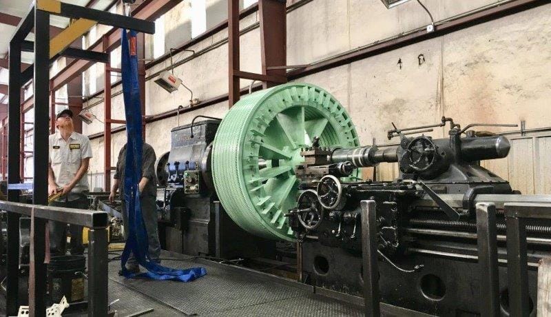 A large green stator core set up on a lathe, with two technicians working alongside