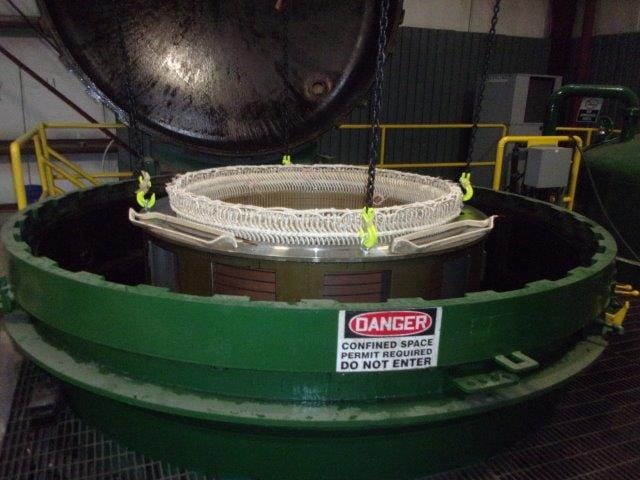 A wound stator being lowered by crane into a vacuum pressure impregnation tank